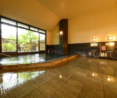 Indoor communal onsen with tiled floor, washing stations and garden view at YufuinOnsenRyokan Mebaeso Ōita