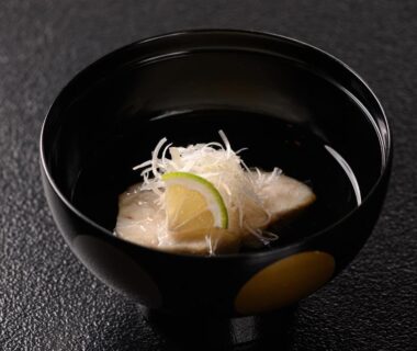 Black lacquer bowl with clear broth, white fish, shredded garnish and citrus slice at ryokan