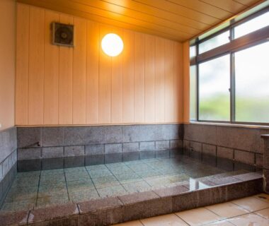 Stone tiled indoor onsen by frosted windows with warm lighting at Yufunoyado Kifu in Ōita