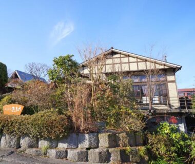 Traditional wooden ryokan exterior at Yufunoyado Kifu in Ōita with stone wall and landscaped shrubs