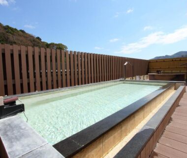 Long rooftop outdoor bath on wooden deck with privacy fence and mountain backdrop at Yugawara Chiyodasou, Kanagawa