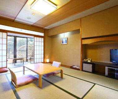 Traditional tatami room with low table, cushions, shoji doors opening to balcony overlooking greenery at Yugawara Chiyodasou