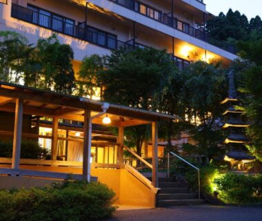Lit wooden entrance and steps at Yugawara Chiyodasou with stone pagoda and balconies in Kanagawa
