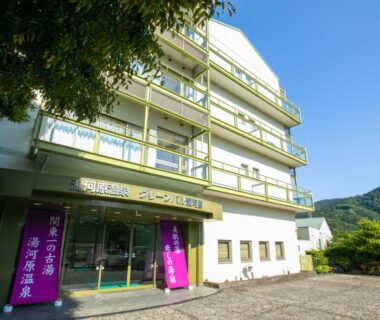 Entrance facade of Yugawara-Onsen GREENPAL YUGAWARA with purple banners and mountain backdrop in Kanagawa