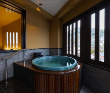 Round soaking tub beside slatted wooden windows with town view in a ryokan guest room