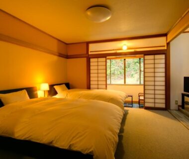Tatami-floored guest room with two beds, shoji screens and garden-facing window at Yugawara-Onsen Komachikan Kanagawa