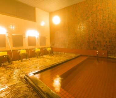 Indoor onsen with tiled walls, large soaking tub and washing stations with stools at Yugawara-Onsen Komachikan, Kanagawa