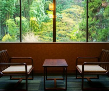 Two wooden chairs and small table facing a large window with lush garden at Yugawara-Onsen Komachikan, Kanagawa