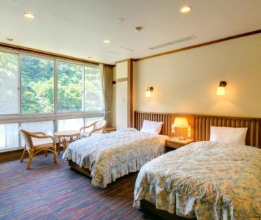 Twin beds and seating by large window overlooking treed hillside at Yugawara-Onsen Manyoso, Kanagawa, Japan