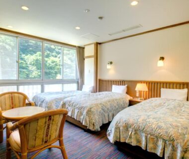 Twin beds with chairs and table by large window at Yugawara-Onsen Manyoso, Kanagawa, Japan
