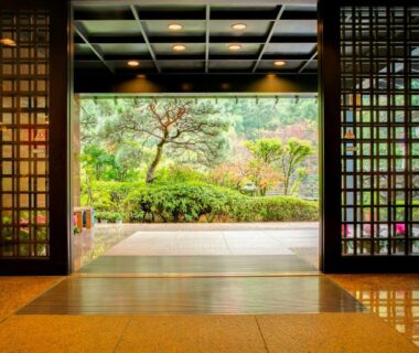 Through wooden lattice doors, polished genkan floor leading to a manicured garden at Yugawara-Onsen SUGINA, Kanagawa