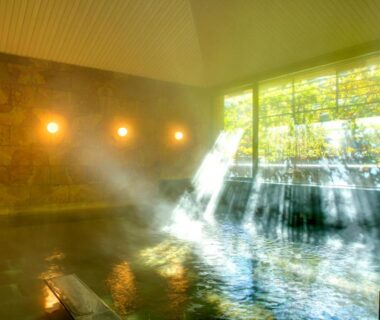 Indoor stone onsen bath with sunlight streaming through large windows and garden view at Yugawara-Onsen SUGINA Kanagawa