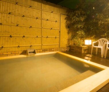 Stone onsen tub on wooden deck with bamboo fence, lanterns and chairs at Yugawara-Onsen SUGINA, Kanagawa
