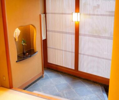 Genkan with stone floor, shoji doors and alcove with single flower at Yugawara Retreat Goen no Mori, Kanagawa