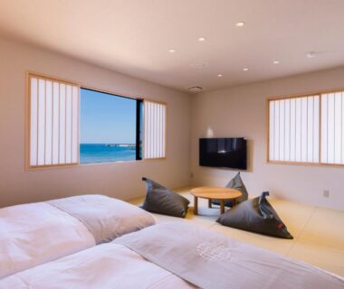 Tatami room with futon beds, low table, cushions and windows framing a coastal view at YuhigauraOnsen Umi no Hana Kyoto