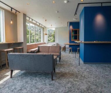 Carpeted lounge with sofas, stools and large windows at YuiLocalZao in Yamagata, Tōhoku