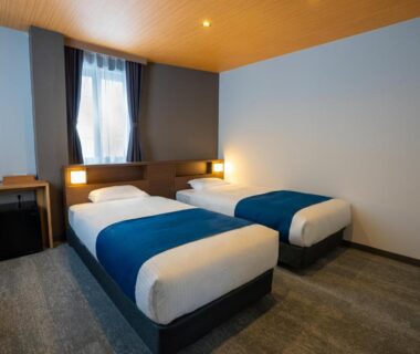 Twin beds with blue runners, bedside lamps, window and desk at YuiLocalZao in Yamagata
