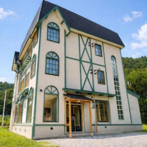 Three-story ryokan YuiLocalZao with half-timbered facade, arched windows and green trim by wooded hills in Yamagata