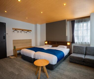 Bright twin bedroom with sofa, small wooden table, coat rack and window at YuiLocalZao in Yamagata