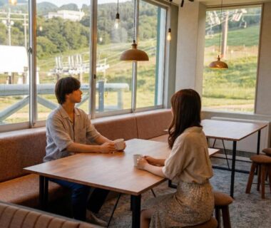 Two guests seated at a lounge table in YuiLocalZao with a hillside view in Yamagata, Tōhoku, Japan