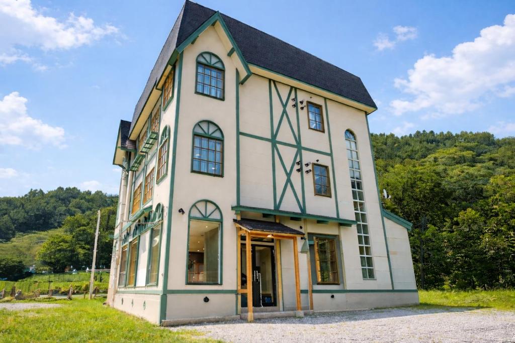 Tudor-style exterior at YuiLocalZao Yamagata Three-story ryokan YuiLocalZao with half-timbered facade, arched windows and green trim by wooded hills in Yamagata