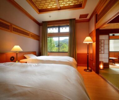 Tatami-floor bedroom with twin beds, shoji screens and adjoining tatami sitting area at Yukaen, Iwate