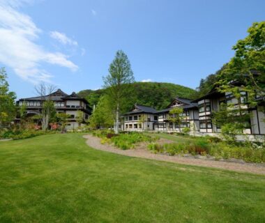 Manicured lawn leading to traditional wooden ryokan buildings surrounded by trees and hills at Yukaen, Iwate