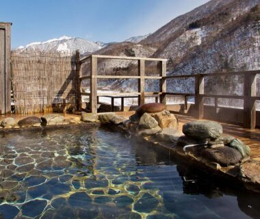 Rock-lined outdoor onsen with wooden deck and snowy mountain views at Yukimurasaki in Gifu