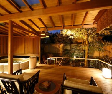 Covered wooden onsen terrace with bath, seating and illuminated garden at night at Yumeguri no Yado Yoshiharu, Shizuoka