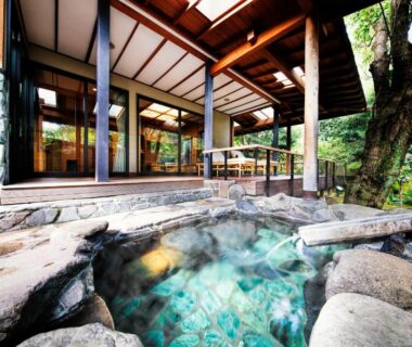 Stone outdoor onsen bath beside wooden terrace and glass doors at Yumeguri no Yado Yoshiharu in Shizuoka