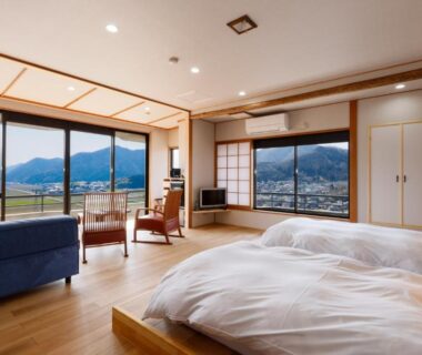 Spacious wooden ryokan room with futon bedding, shoji screens, seating and wide windows overlooking mountains in Hyōgo
