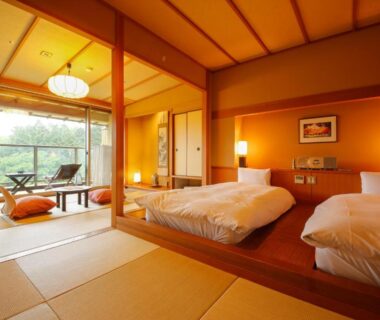 Tatami room with twin beds on raised wooden platform, low table and balcony with greenery at Yumenoian Yuyake Koyake Hyōgo