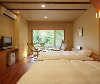 Twin beds with seating area and garden view through sliding doors in a ryokan guestroom