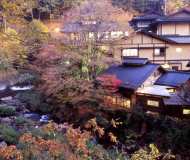 Riverside wooden ryokan Yumerindo with autumn foliage and lit windows in Kumamoto, Kyushu