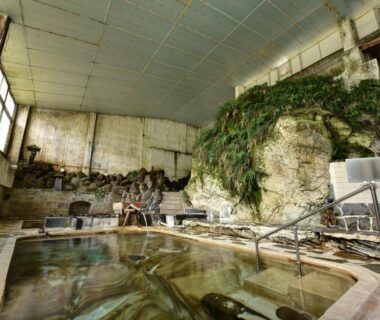 Indoor onsen bath with natural rock wall, wooden stools and handrail at Yumorinoyado Sannozyou, Yamagata Tōhoku Japan