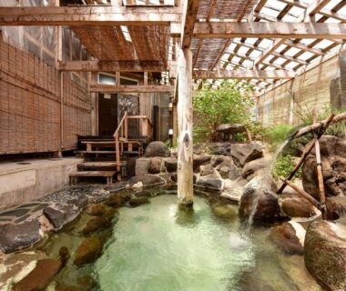 Stone-lined onsen bath with wooden pergola and bamboo screens at Yumorinoyado Sannozyou in Yamagata
