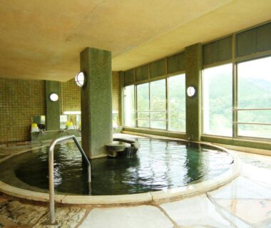 Large tiled indoor onsen bath with handrail and large windows at Yumoto Choseikan, Gunma