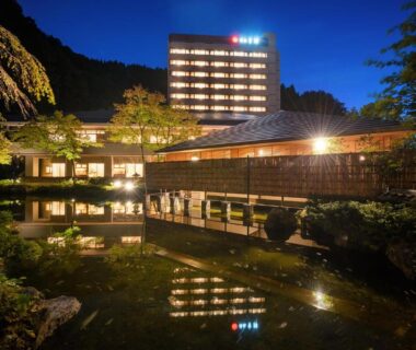 Evening view of Yumoto Kissho's illuminated wooden buildings reflected in a calm pond and garden, Miyagi