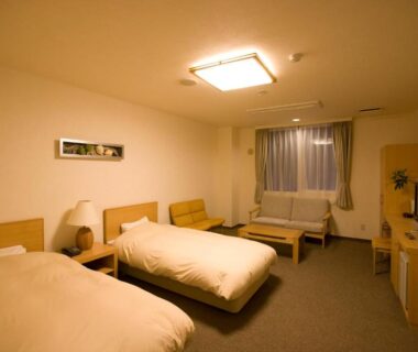 Spacious twin room with two beds, sofa seating, TV and soft lighting at Yumoto Koganeyu in Hokkaidō