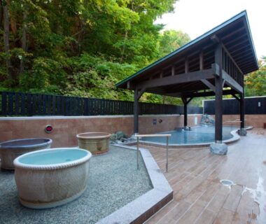 Stone outdoor onsen tubs and covered wooden bath area at Yumoto Koganeyu in Hokkaidō