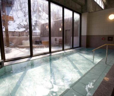 Indoor onsen pool with large glass windows at Yumoto Koganeyu in Hokkaidō