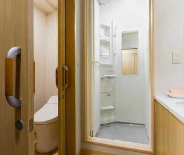 Compact washroom with separate toilet, enclosed shower stall, wood flooring and light wooden doors at Yumoto Noboribetsu Hokkaidō