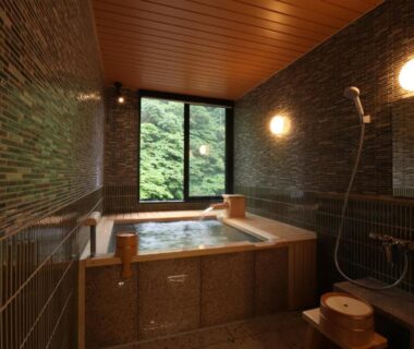 Tiled indoor bathing room with wooden tub, shower area and forest view at Yumoto Ueyama, Hyōgo