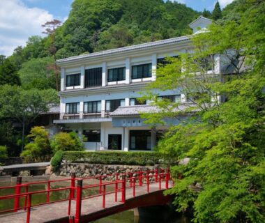 Red bridge leading to Yumoto Ueyama beside a river and forested hillside in Hyōgo, Kansai