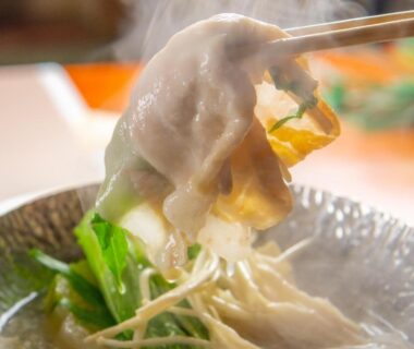 Steaming nabe with greens and mushrooms, chopsticks lifting ingredient at Yumotoya, Nagano, Chūbu