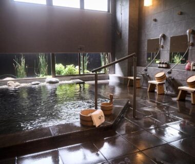 Stone-lined indoor onsen pool with wooden stools and shower stations at Yumura Onsen MIDORIYA, Hyogo, Kansai