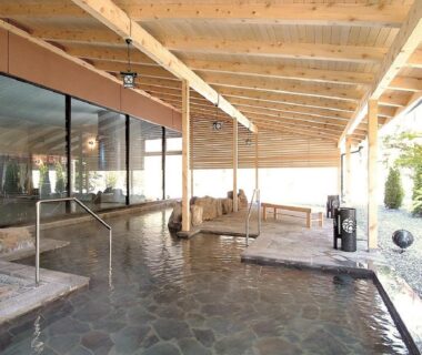 Covered stone-floor onsen bath with wooden beams, metal handrails and sheltered walkway at the ryokan in Hokkaidō