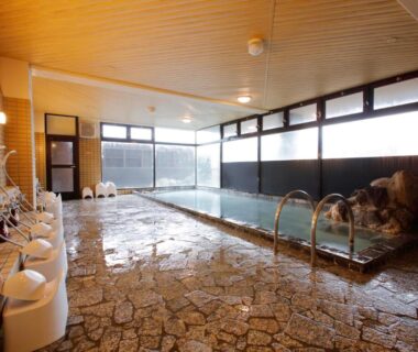 Large indoor onsen with stone floor and washing stations at Yunokawa Onsen Emi Hakodateya in Hokkaidō