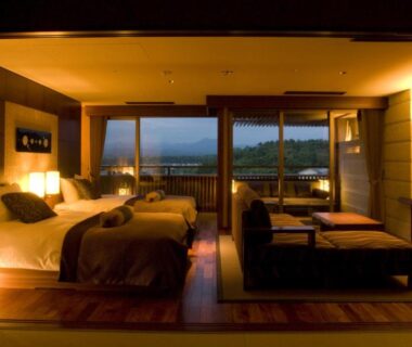 Warm-lit room with two beds, low seating and shoji screens at Yunokuni Tensyo in Ishikawa, Chūbu, Japan