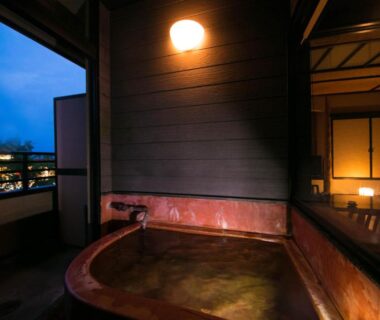 Wooden soaking tub on balcony beside shoji screens and tatami room at dusk, Yunosato Hayama, Ōita Japan